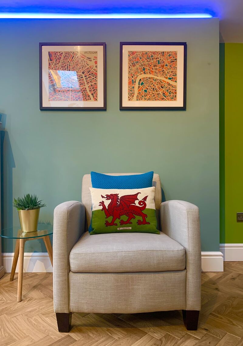Armchair under two framed city prints on a teal wall