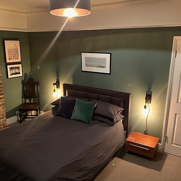 Bedroom painted dark green beside a bare brick chimney breast