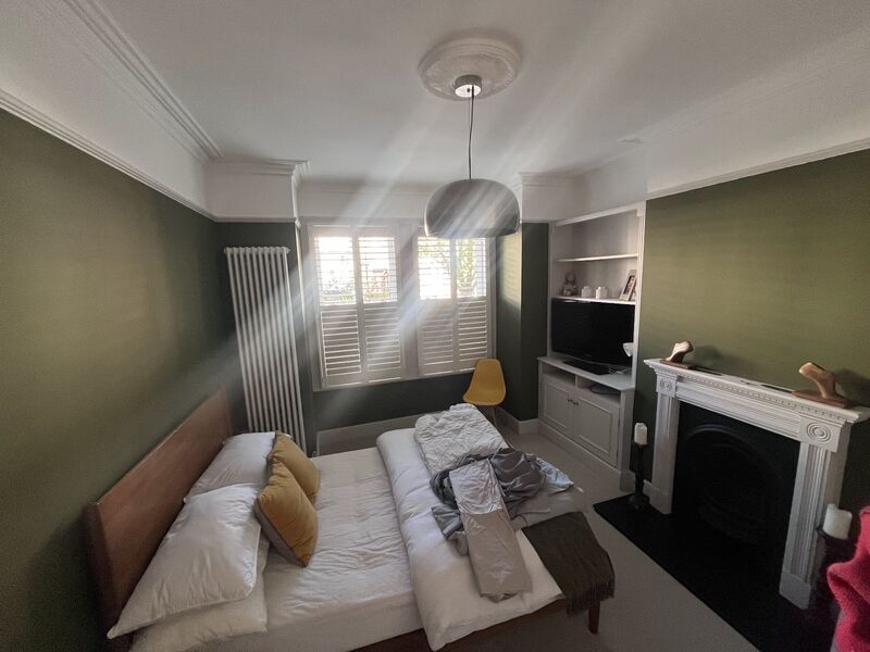 Bedroom painted in olive green with a white fireplace and shutters