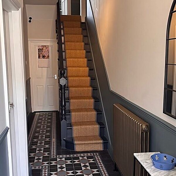 Hallway with a patterned tiled floor, a stair runner and grey panelling