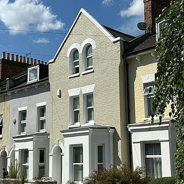 Front of a Victorian terraced house, painted cream with white window surrounds