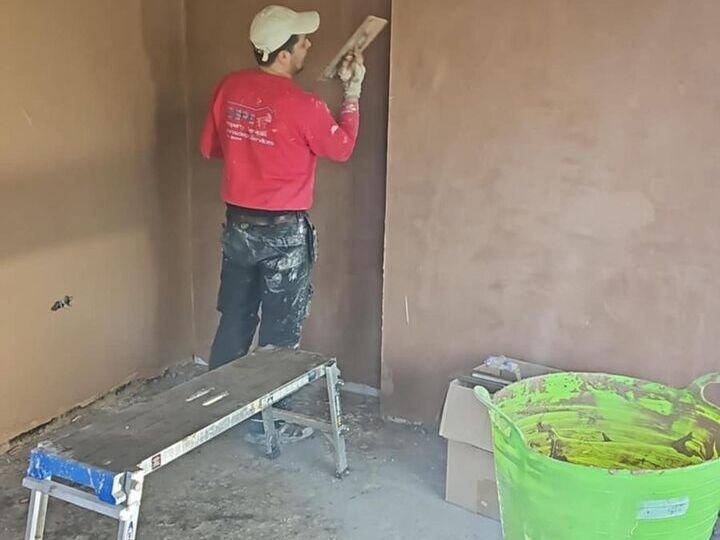 Plasterer skimming the walls of a room, with fresh plaster drying